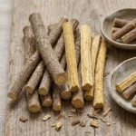 Bâtons de réglisse bruts (Glycyrrhiza glabra) coupés sur un support en bois, illustrant la racine utilisée pour le confort de l'estomac
